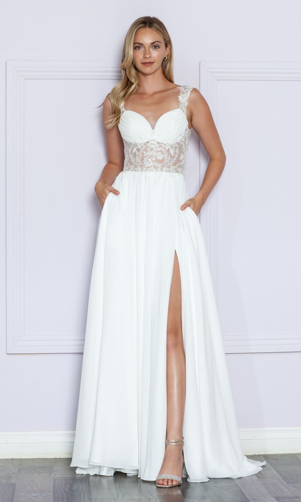 A woman in the Sheer-Lace Bodice Long White Formal Dress 9376, featuring a side slit and pockets, stands against a light purple wall.